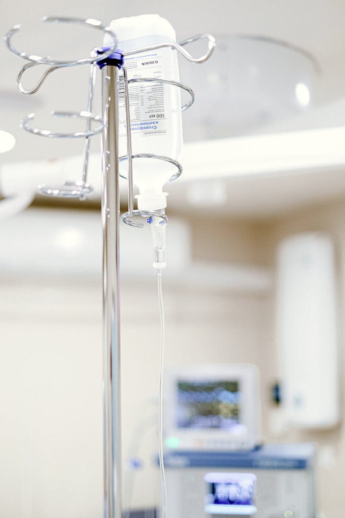 About Close-up of an IV drip in a sterile hospital setting with background medical equipment.