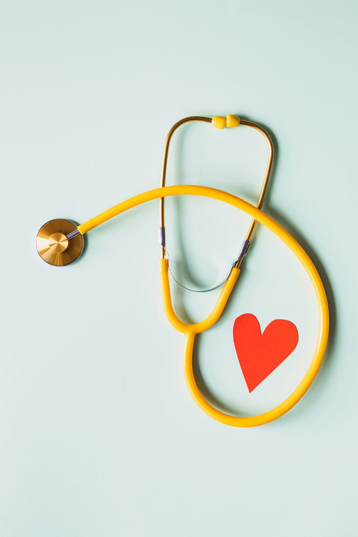 About Yellow stethoscope arranged with a red heart cutout on a light green background, symbolizing heart health.